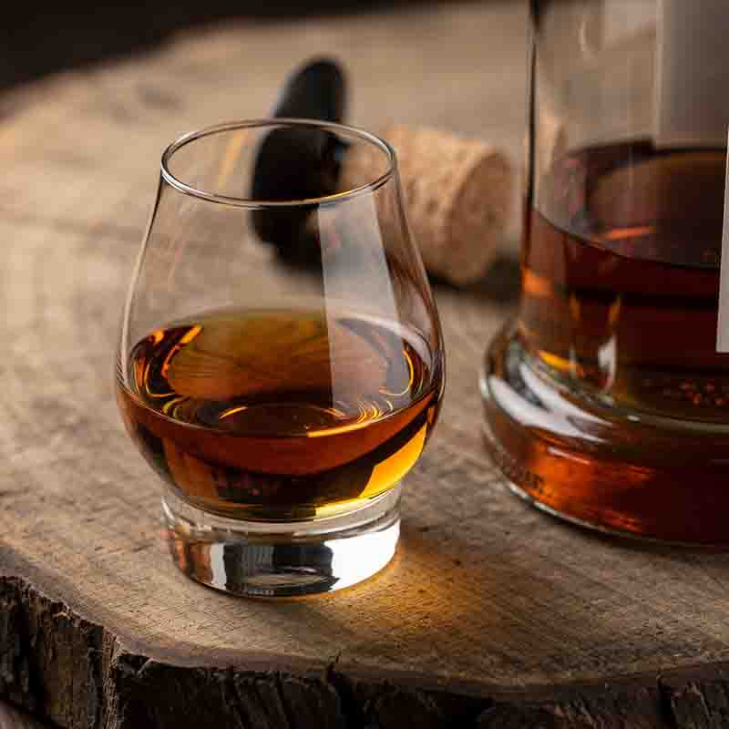 Ein elegantes Single Malt Whisky Glas auf einem rustikalen Baumstamm-Untersetzer.